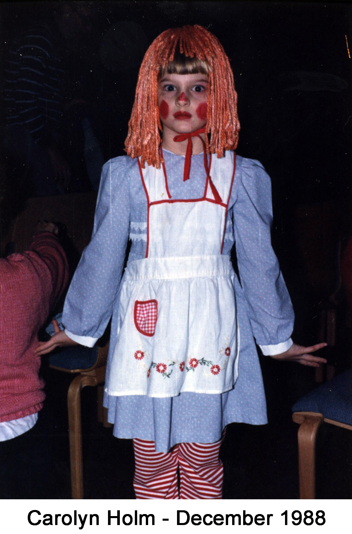 She is posed for the camera with her checks bright red, an orange wig, a             blue dress, with red-and-white candy cane stockings
