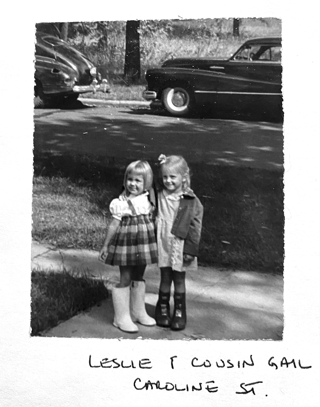 The two girls are standing on a sidewalk