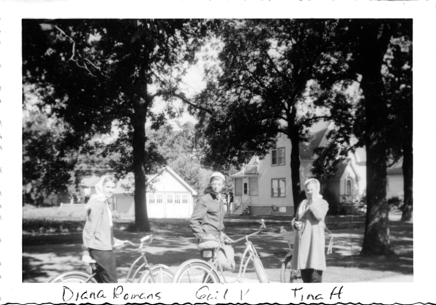 The three girls are looking toward the camera. 
               They have the old-fashioned, balloon-tire bikes. 