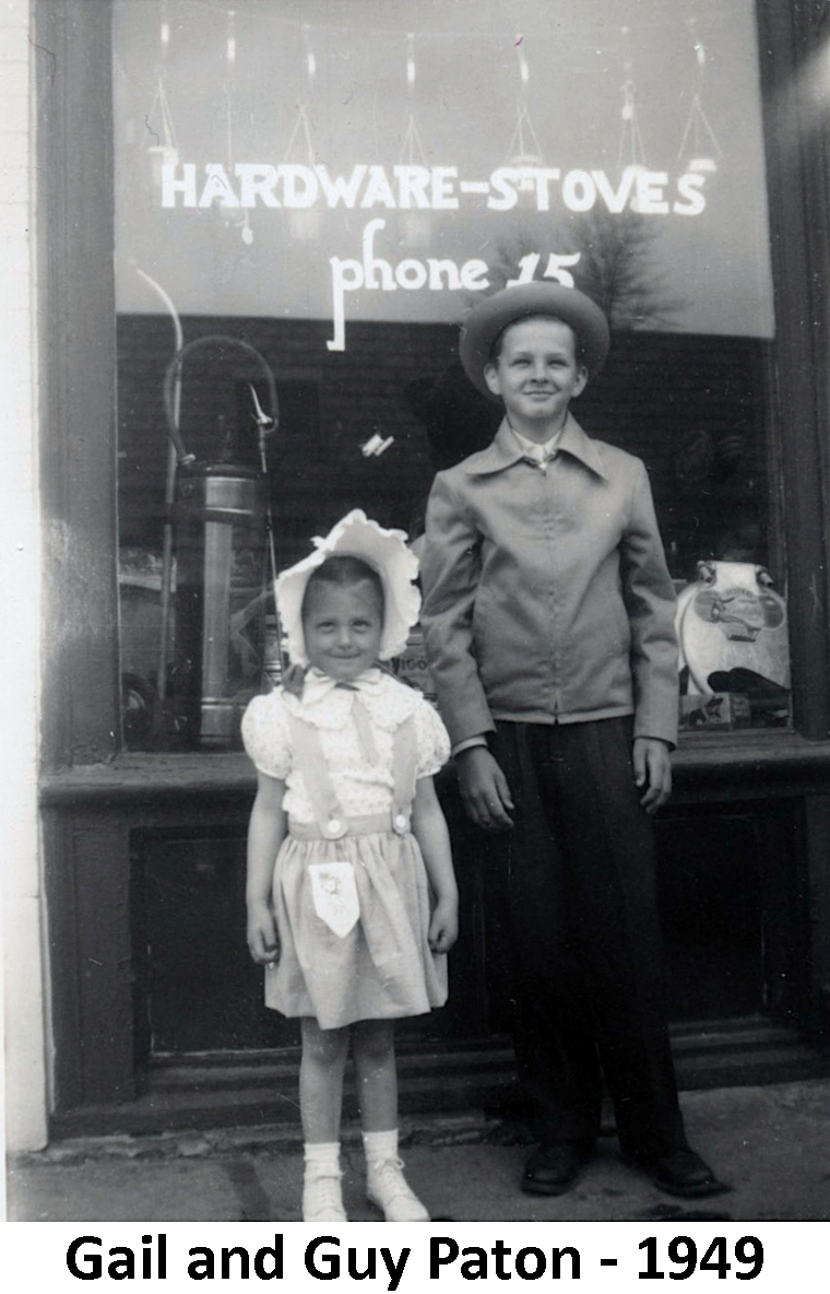 Gail and Guy Paton standing in front of the hardware store window. 
             Phone number 15.