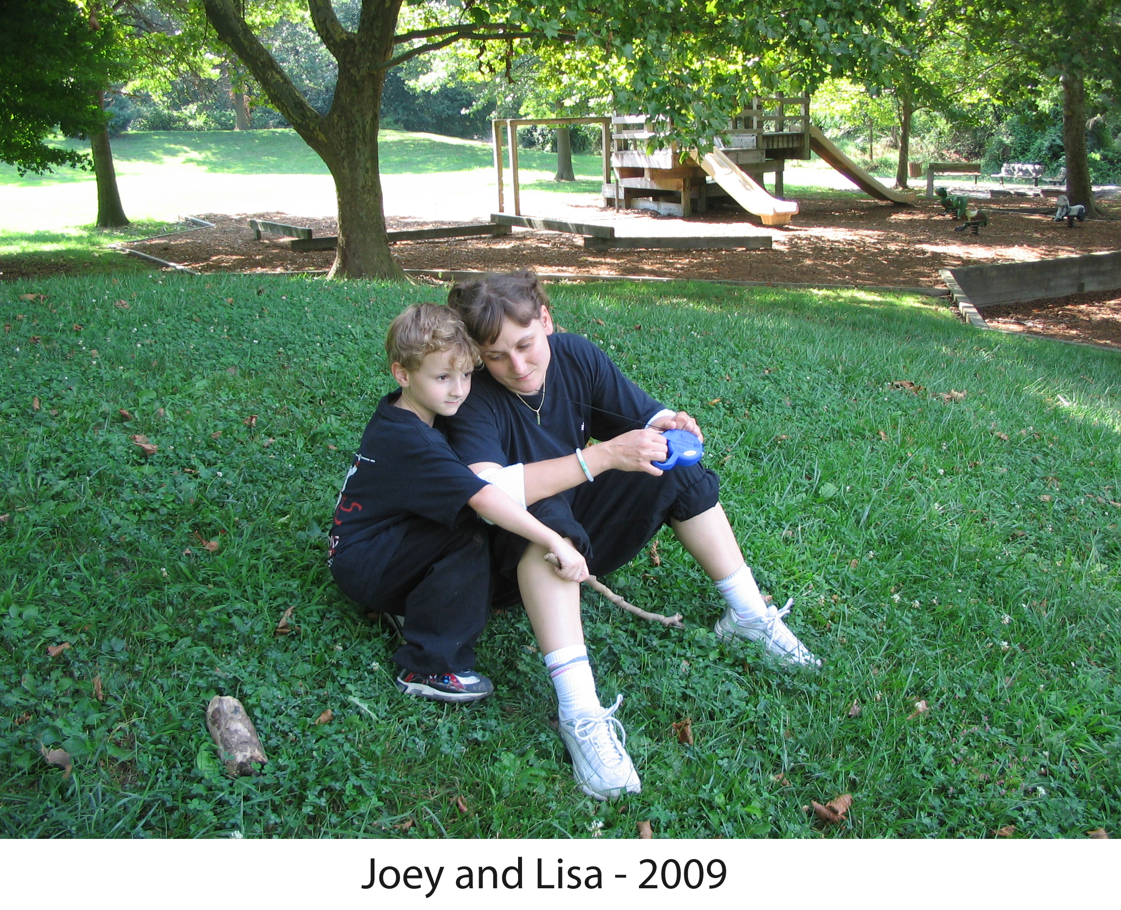 Joey and Lisa sitting together
     on the grass in front of the playground in our Tot Lot