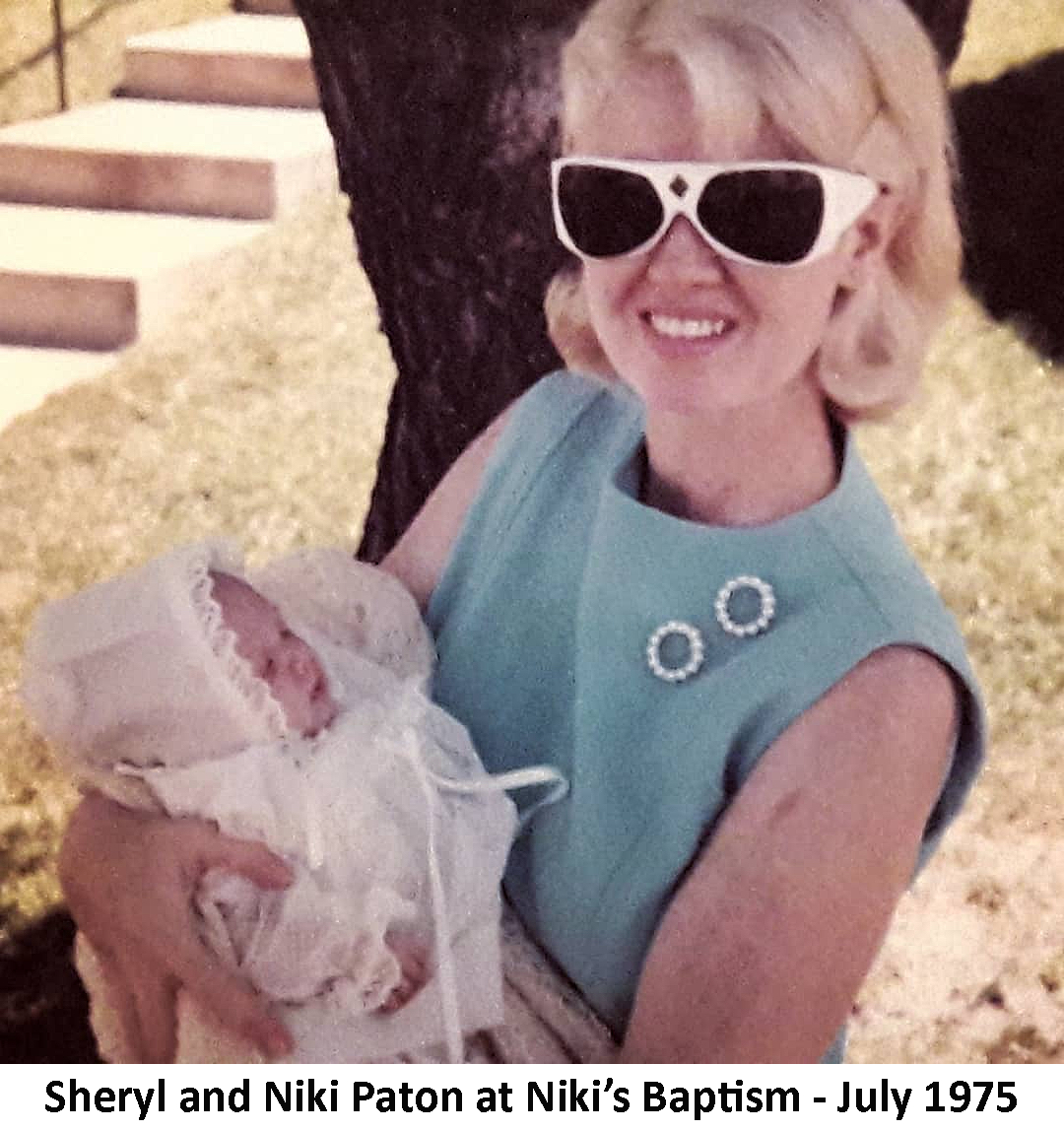 Sheri Paton is holding Niki at Niki's baptism. 
               Sheryl is wearing sunglasses.