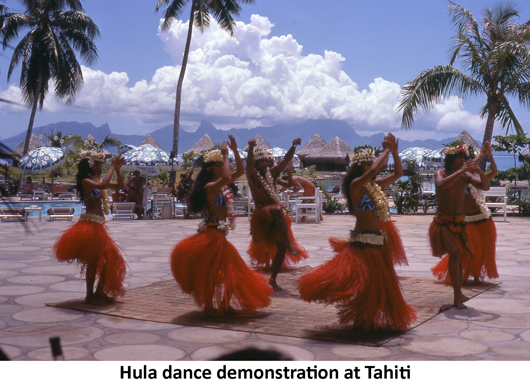 Six Tahitian women and two men in red skirts demonstrate a hula dance