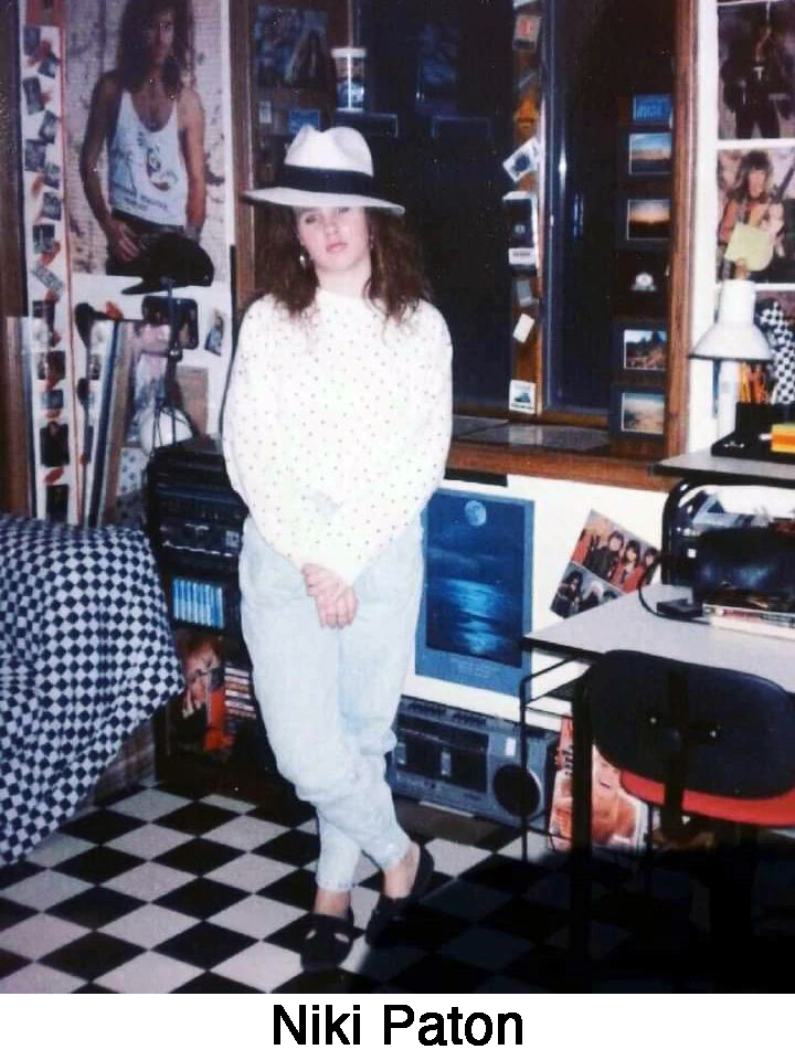 Niki standing in a room with photos, posters on the walls, and a boombox