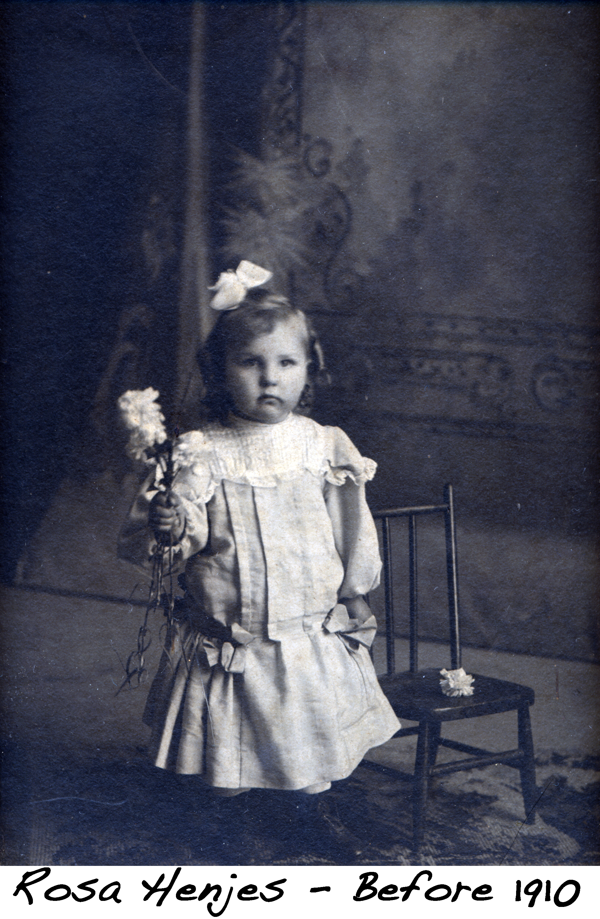 Baby Rose Henjes holds a flower and has a bow in her hair for her portrait