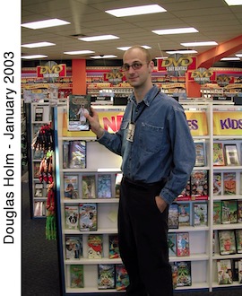 Doug Holm is standing next to shelves of videos and holding a box