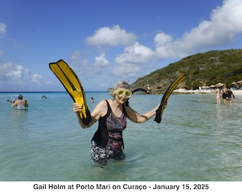 Gail Holm is standing hip deep in the water, wearing her mask and snorkle, and
               holding her swim fins. 