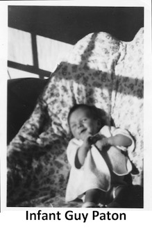 The smiling infant Guy Paton is lying on a leopard-spotted blanket 