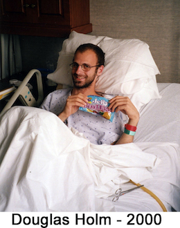 Doug Holm lying back on a pillow in a hospital bed and smiling with a bag of candy