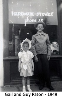 Gail and Guy Paton standing in front of the hardware store window. 
             Phone number 15. 