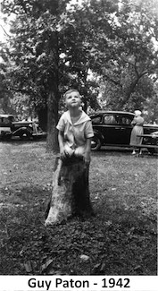 Guy Paton kneeling on a stump at a picnic