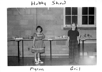 Myrna and Gail standing next to their tables at a hobby show