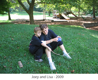 Joey and Lisa sitting together on the grass in front of the playground in our Tot Lot