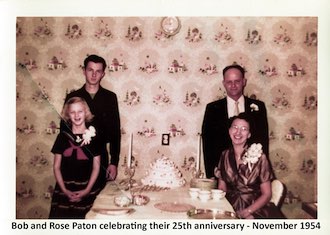 The Paton family is dressed nicely. Gail and Rose are seated at a table
          with a fancy cake on it and Guy and Robert are standing in behind them.