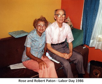 Rose and Bob Paton are sitting together in a room in their home.               They are looking at the camera.