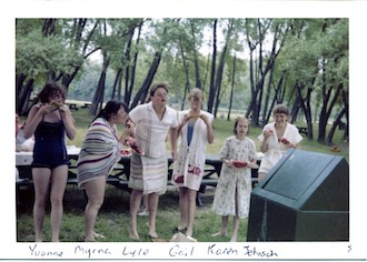 Five girls in swim suits and towels, lined up, eating watermelon and 
             spitting the seeds