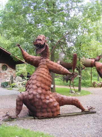 The marsh dragon is sitting on the ground and is
               maybe 10 feet high. It has a club in its left hand.
               Its open mouth shows large teeth. It has two
               mesh wings. It is rust colored.