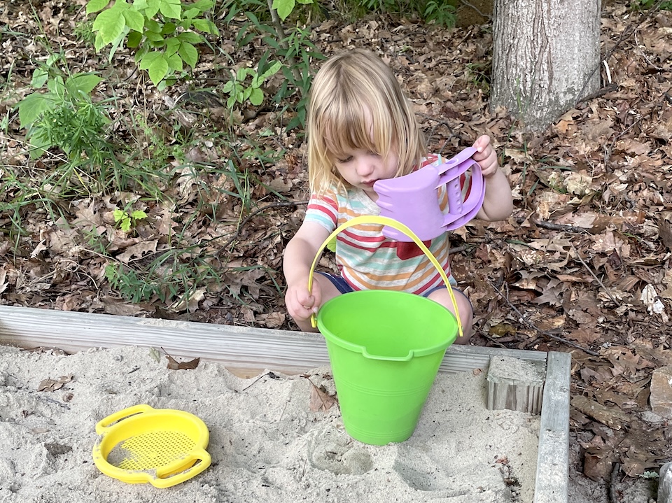 Morgan plays with a shovel and a bucket in the sandbox 